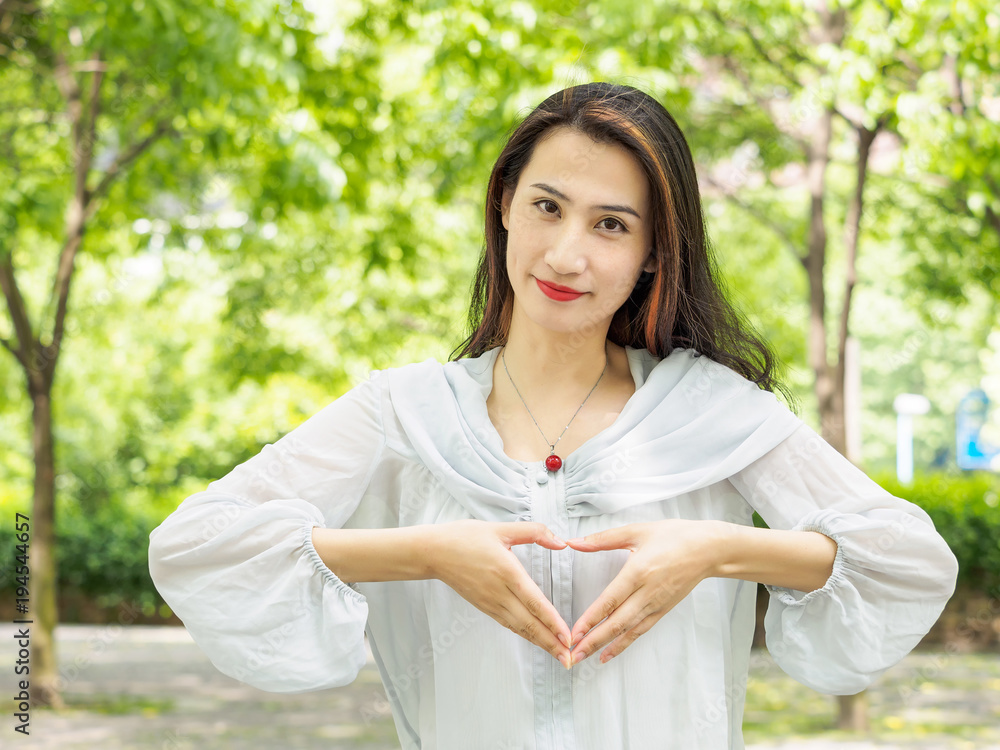 Beautiful young brunette Asian woman make a heart gesture near her heart. Outdoor fashion portrait of glamour young Chinese stylish lady. Emotions, people, beauty and lifestyle concept. Beautiful young brunette Asian woman make a heart gesture near her heart. Outdoor fashion portrait of glamour young Chinese stylish lady. Emotions, people, beauty and lifestyle concept.