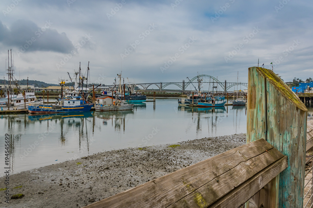 a small harbor in Oregon with boats, reflections in the water, sky, bridge in background