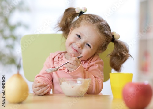 Funny child eating healthy food with a spoon at home