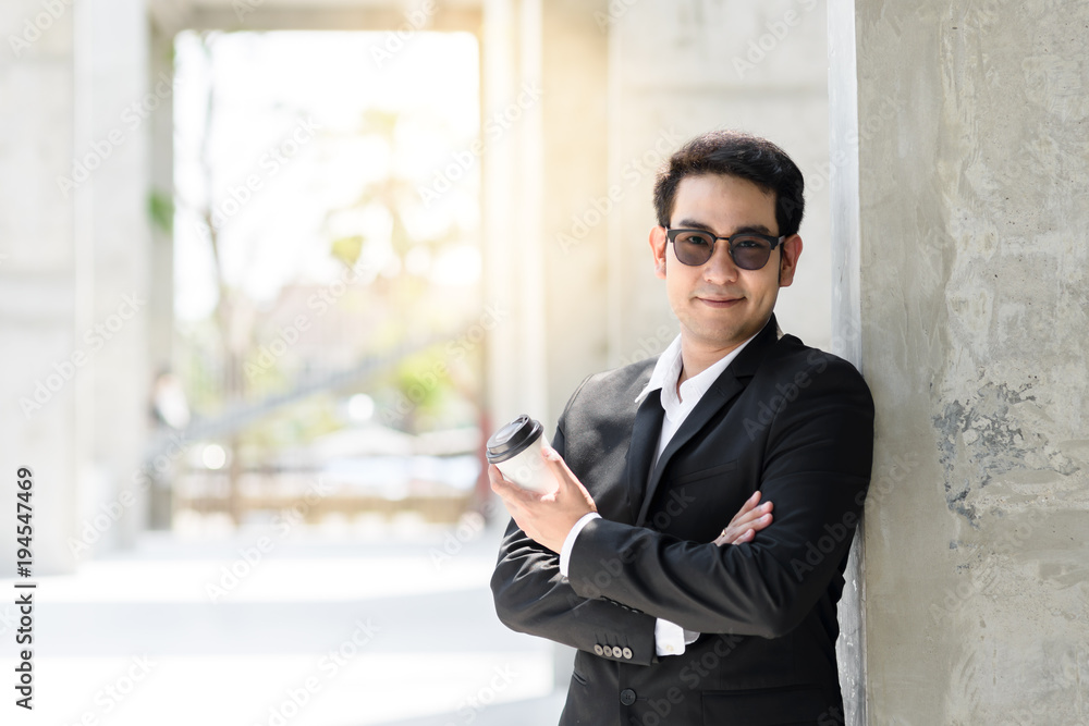 Asian modern businessman holding coffee cup and standing along the building, lifestyle concept. Asian modern businessman holding coffee cup and standing along the building, lifestyle concept.