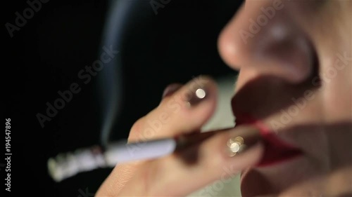 Woman with red lips smokes  cigarette and exhales smoke . Blurred face .Extreme close up