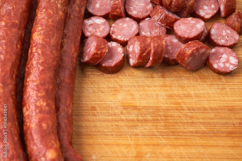 Thin smoked sausage whole and sliced on a wooden background. Close-up. Thin smoked sausage whole and sliced on a wooden background. Close-up.