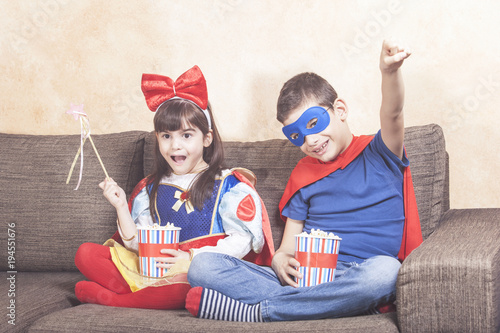 Happy kids dressed up as super heroes and fantasy characters watching TV