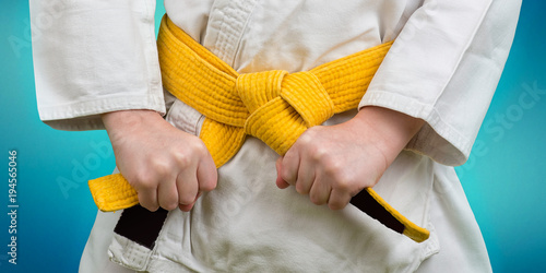 Hands tightening yellow belt on a teenage dressed in kimono for martial arts photo