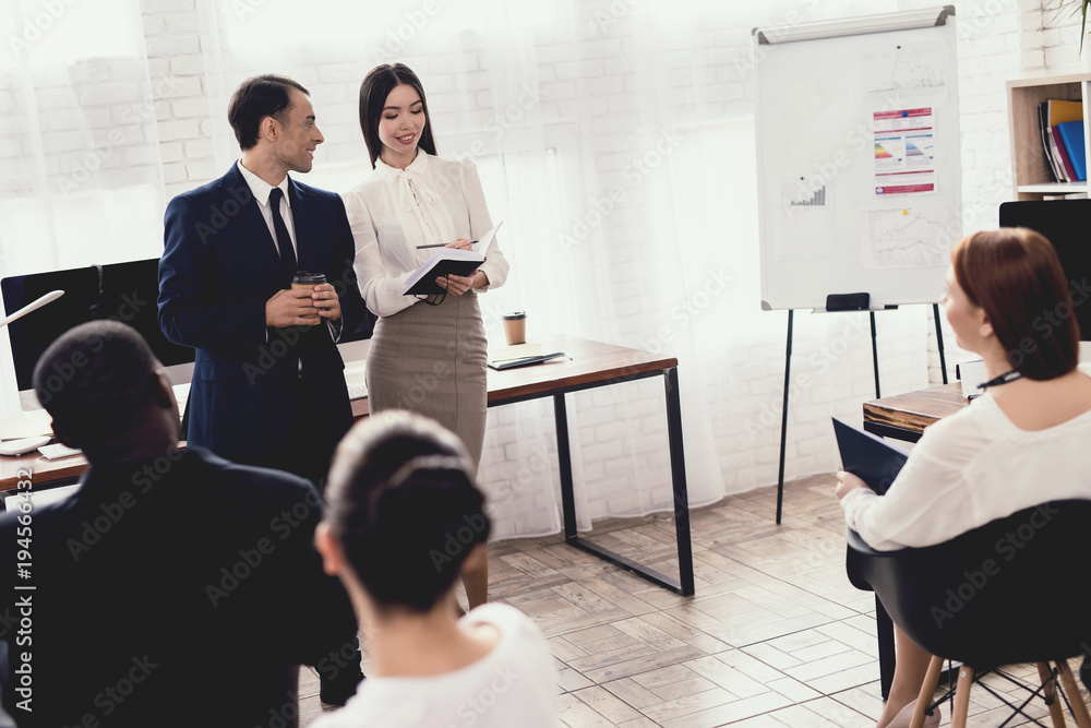 A man of Arab appearance and an Asian girl are lecturing before other office workers. A man of Arab appearance and an Asian girl are lecturing before other office workers.
