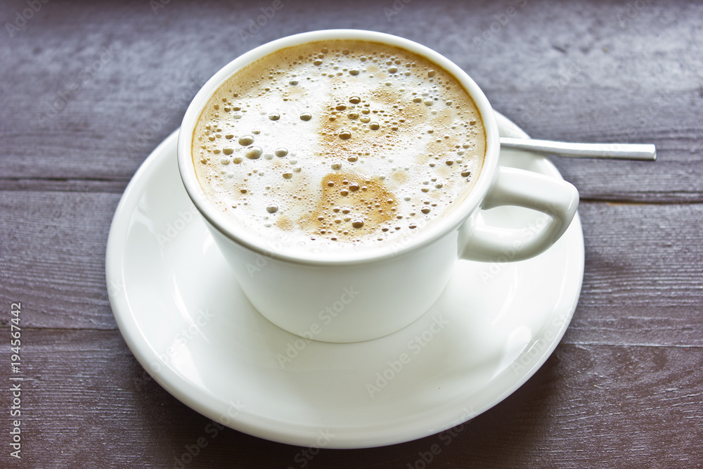 Coffee latte with milky foam and bubbles in a white porcelain cup on a saucer on a wooden brown table. Coffee latte with milky foam and bubbles in a white porcelain cup on a saucer on a wooden brown table.