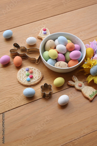 Easter background. Multicolored choccolate eggs, cookies in shape of bunny, bell and egg,and decoration on wooden table
