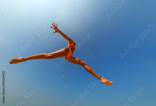 Carefree woman in bikini jumping on the beach with arms outstretch