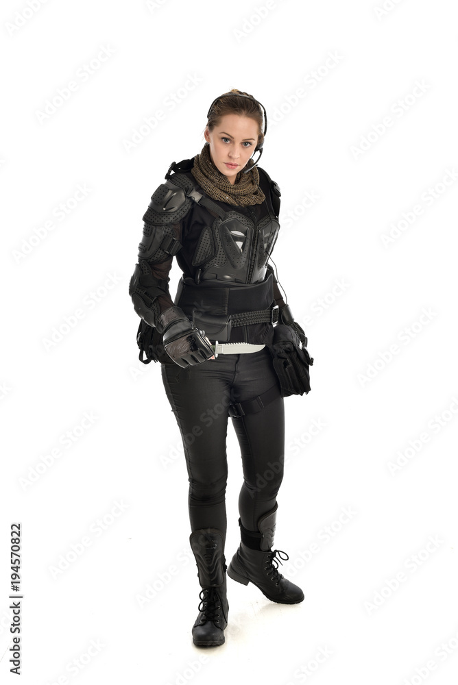 Fototapeta premium full length portrait of female soldier wearing black tactical armour, holding a remote knife, isolated on white studio background.