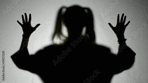 Silhouette of a creepy halloween girl ghost with pigtails hairstyle putting hands on screen and scratching