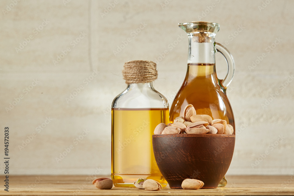 Aromatic oil in a glass jar and bottle with pistachio in bowl on wooden table, close-up Aromatic oil in a glass jar and bottle with pistachio in bowl on wooden table, close-up
