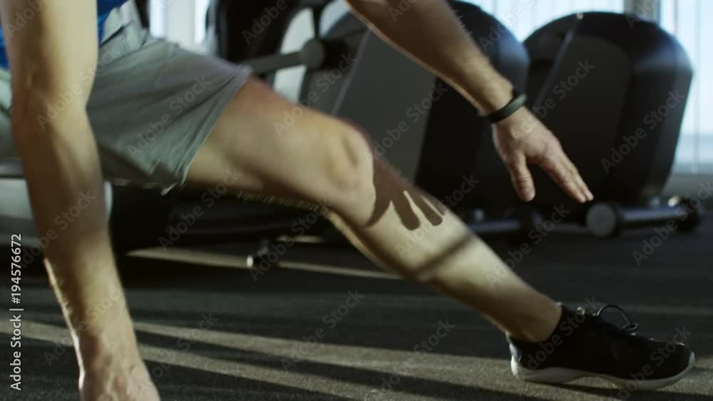 Close up tracking shot of mature man doing adductor stretching exercises at empty gym Close up tracking shot of mature man doing adductor stretching exercises at empty gym