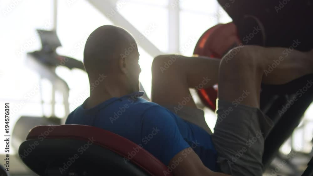 Medium shot of middle-aged man working out with leg press machine at the gym during sunset Medium shot of middle-aged man working out with leg press machine at the gym during sunset
