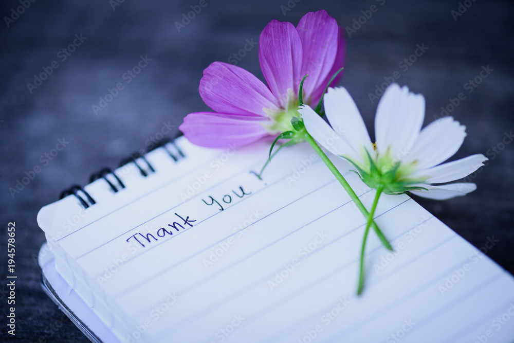 Naklejka premium Thank You text on a white page note book with romantic white flower on wooden background.