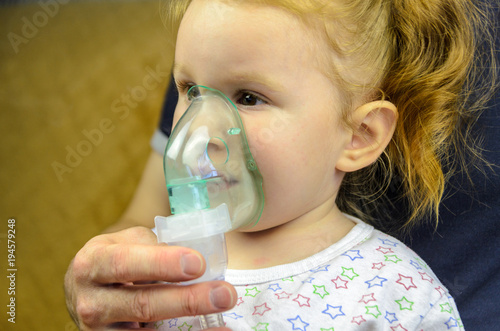 medical inhalation treatment - Little girl breathes with face mask of modern jet nebulizer