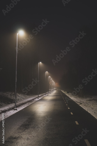 Lonely foggy park alley at winter night.