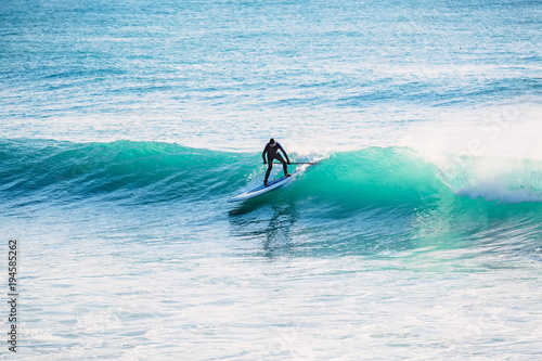 Photography Surfer on stand up paddle board on wave. Winter surfing in ocean