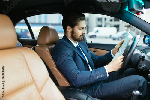 Businessman reading newspaper in his car, while waiting for his assistent.