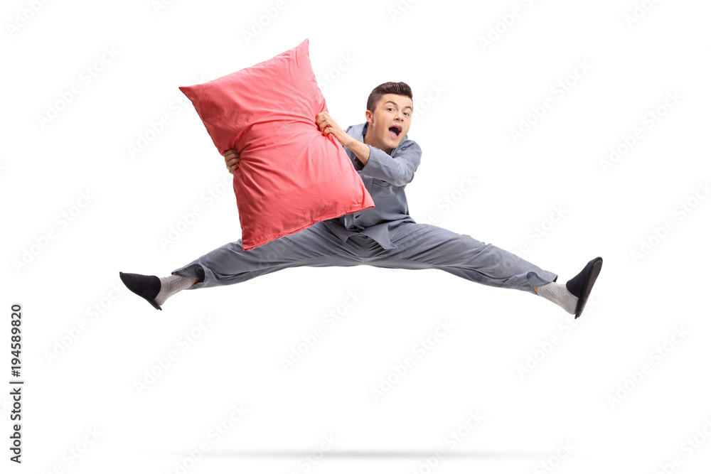Overjoyed teenager in pajamas holding a pillow and jumping - obrazy, fototapety, plakaty 
