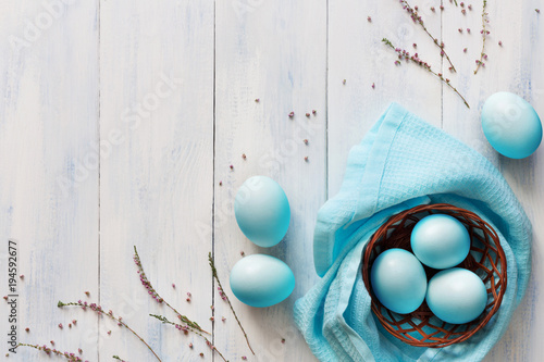 Photography Blue easter eggs in small basket on wooden background