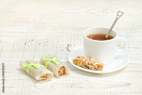 Cup of tea and few bar of muesli. White wooden background