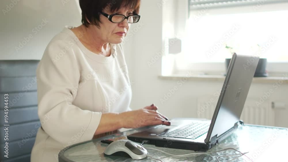 An elderly woman pays bills with a laptop and a bank card. Online payments. Hyperopia An elderly woman pays bills with a laptop and a bank card. Online payments. Hyperopia