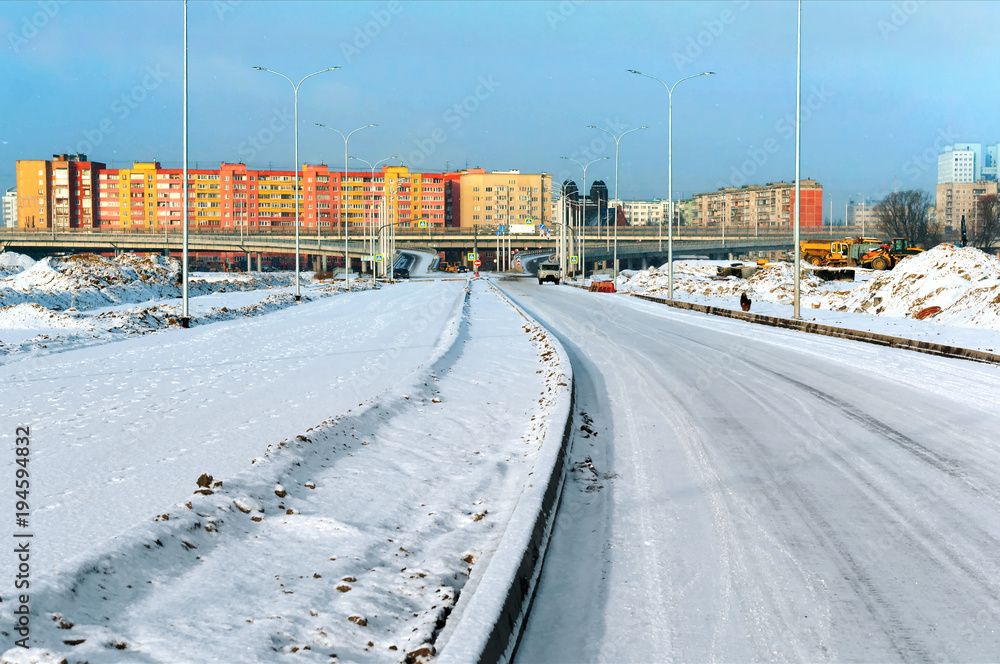 Snow-covered road to the city. Road junction overpass and high-rise buildings in the winter in the snow.