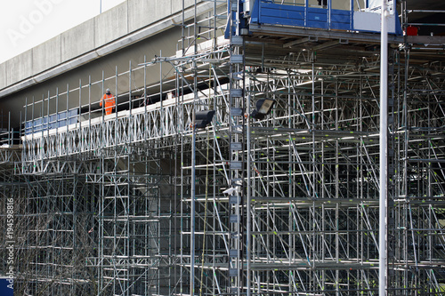 Highway maintenance. Scaffolding structure allowing workers to inspect and repair the underneath of a long concrete motorway flyover/bridge. An engineer checking a highway bridge from a gantry.