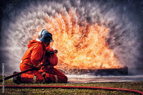 Firefighter in fire fighting suit spraying water, Firemen fighting  raging fire with huge flames of burning, Fire prevention and extinguishing concept