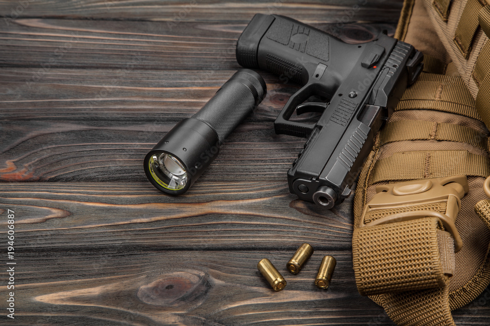 Obraz premium black pistol, flashlight and cartridges on a brown wooden