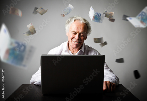 Old man using a laptop. Old man in white earns Euro on the internet.