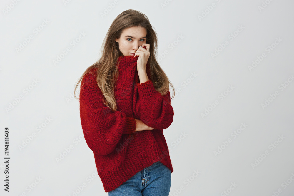 Girl hugged boyfriend and smells his perfume on her sweater. Portrait of sensual good-looking european model in trendy outfit pulling collar on face while standing against gray background. Girl hugged boyfriend and smells his perfume on her sweater. Portrait of sensual good-looking european model in trendy outfit pulling collar on face while standing against gray background.