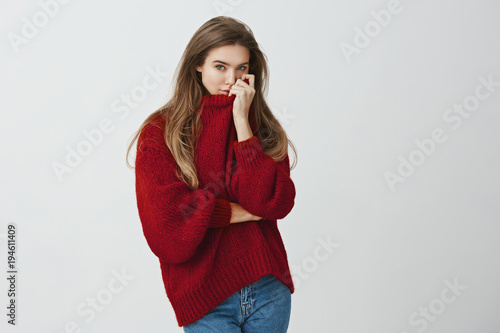 Girl hugged boyfriend and smells his perfume on her sweater. Portrait of sensual good-looking european model in trendy outfit pulling collar on face while standing against gray background.