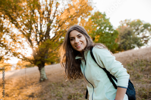Young beautiful woman on a hill in the forest with backpack in the autumn season, at sunset, looking happy and smiling 