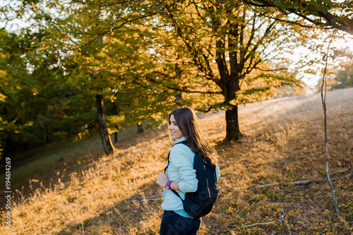 Young beautiful woman on a hill in the forest with backpack in the autumn season, at sunset, looking happy and smiling  © vladteodor