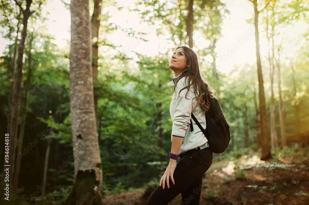 Pretty young woman smiling happy carrying backpack in the forest on sunset light in the autumn season. Pretty young woman smiling happy carrying backpack in the forest on sunset light in the autumn season.