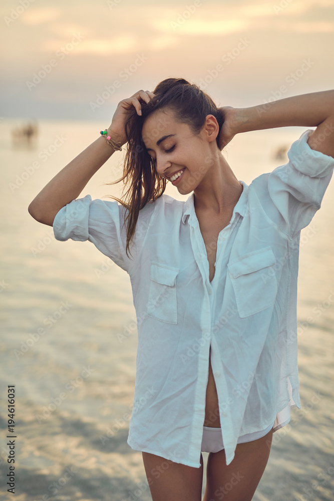 beautiful sexual woman in white shirt and bikini walking on the beach against the sea and sunset beautiful sexual woman in white shirt and bikini walking on the beach against the sea and sunset