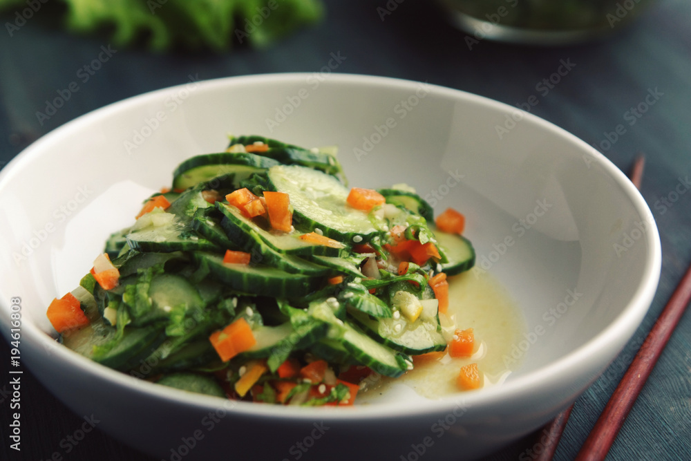 Asian cucumber salad on the white plate. Chopsticks. Chinese cuisine. Bell pepper, cucumber and sesame seeds. Vegetarian dish. Asian cucumber salad on the white plate. Chopsticks. Chinese cuisine. Bell pepper, cucumber and sesame seeds. Vegetarian dish.