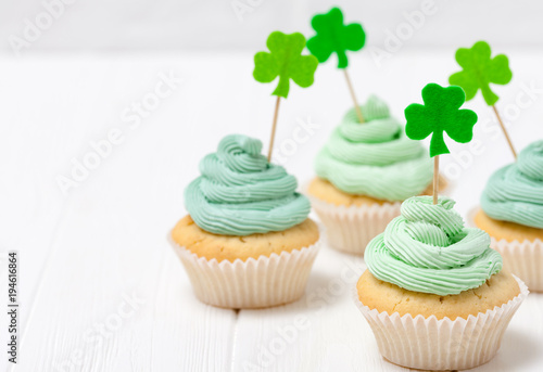 St. Patrick's Day theme colorful horizontal banner. Cupcakes decorated with green buttercream and craft felt decorations in form of shamrock leaves on white background. Copy space. For greeting card