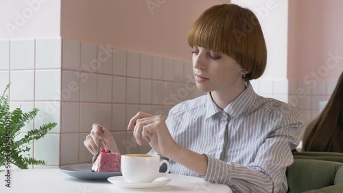 Young beautiful red-haired girl sitting in cafe, eating cake and drinking coffee. 60 fps photo