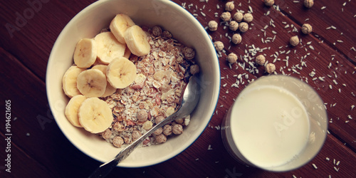 Healthy breakfast. Granola bowl with banana, raisins and nuts. And a glass of milk on the wooden background. Top view. Close up photo. Sweet vegan dish. Morning oatmeal closeup.