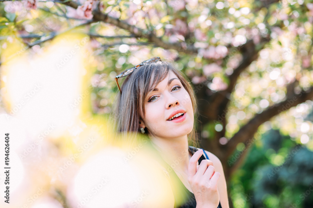 Young beautiful woman near sakura blooming tree. Pink flowers, spring and youth concept. Stylish girl smiling. Young beautiful woman near sakura blooming tree. Pink flowers, spring and youth concept. Stylish girl smiling.