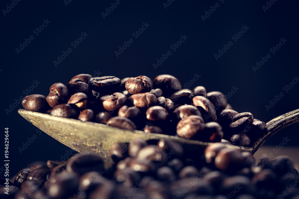 Grains of coffee lie in an old antique spoon. Unusual photo low key. Grains of coffee lie in an old antique spoon. Unusual photo low key.