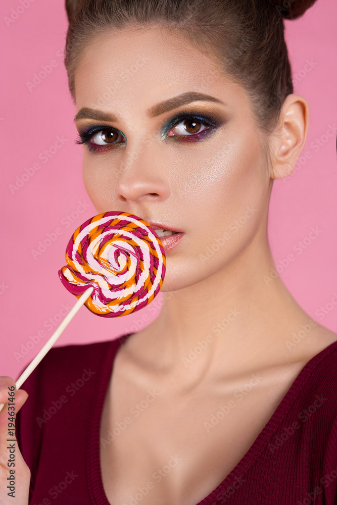 beautiful girl eats candy on a stick on an isolated pink background. advertising for a confectioner's shop