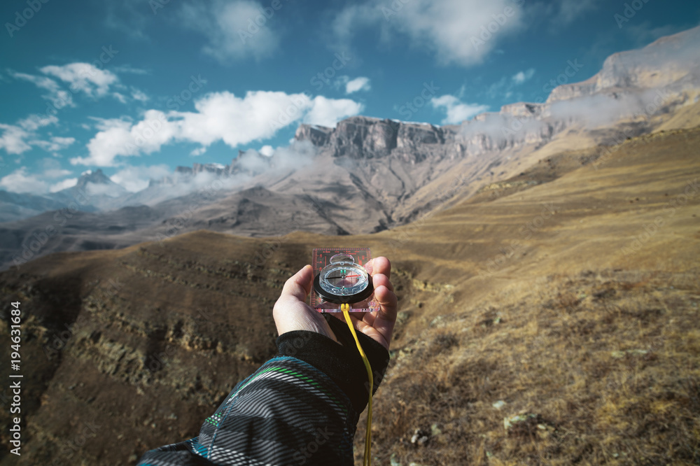 Viewpoint shot. A first-person view of a man's hand holds a compass against the background of an epic landscape with cliffs hills and a blue sky with clouds