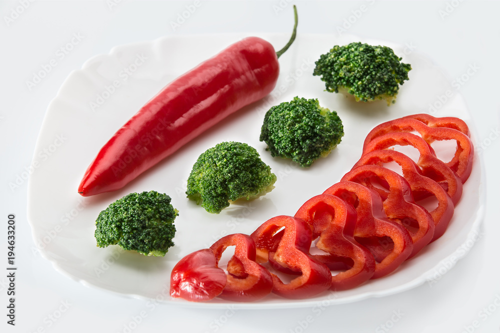 Slices of bell pepper, chili, broccoli on a white plate on a white background Slices of bell pepper, chili, broccoli on a white plate on a white background