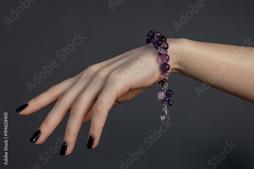 женская кисть руки с черным лаком на ногтях и красивым браслетом из сиреневых драгоценных камней 