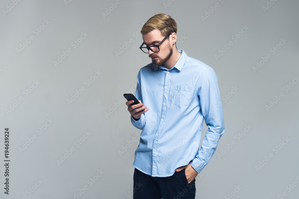 Serious and handsome. Young business man messaging on his mobile phone. Grey background. Serious and handsome. Young business man messaging on his mobile phone. Grey background.