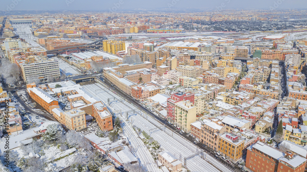 Aerial view of the Tuscolana station in Rome, Italy. Around the tracks there are the palaces and streets of the Italian city. The railroad tracks are made of steel. Everything is covered by snow on 02