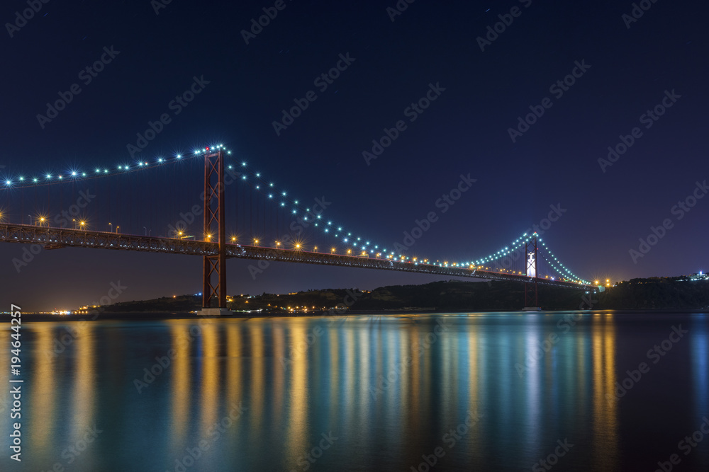 Fototapeta premium Beautiful and serene view of the Tagus River and the 25 of April Bridge (Ponte 25 de Abril) at night, in Lisbon, Portugal; Concept for visit Lisbon
